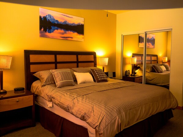 A hotel room with a large bed, two bedside tables with lamps, a mirror, and a painting of a mountain landscape.