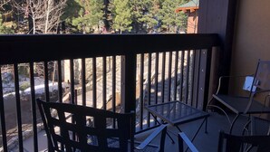 A balcony with a view of trees and a building. There are two metal chairs and a small table.