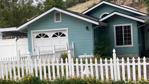 Ein zweistöckiges Haus mit weißem Zierzaun, einer Garage und einem kleinen Garten mit gelben Blumen.