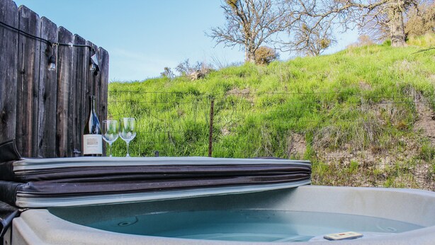 Ein Whirlpool mit Holzterrasse und einer Weinflasche, umgeben von einer grünen Hügelkuppe.