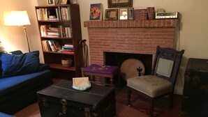 Un salon chaleureux avec un canapé bleu, un fauteuil en bois, une cheminée, une bibliothèque et une valise ancienne.