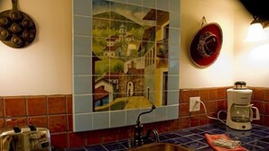 Une cuisine avec un mur recouvert de carreaux, un évier, une machine à café et une assiette décorative accrochée au mur.