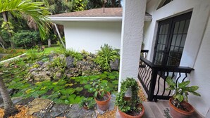 Un jardin avec un bassin, des plantes en pot et un bâtiment blanc doté d’une balustrade noire.