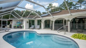 Une piscine entourée de parois en verre, des chaises longues et un espace patio couvert.