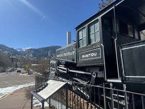 A black train engine with "Manitou & Pike's Peak" and "Manitou" signage, set against a snowy mountain backdrop. - Easy Walk to Shops, Restaurants and parks. Pet Friendly with fenced backyard. (Colorado Springs)