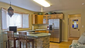 Una cocina con una isla de piedra, sillas de madera, un refrigerador de acero inoxidable y armarios de madera.