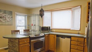 Una cocina con una isla de piedra, electrodomésticos de acero inoxidable, armarios de madera y una ventana con persianas.