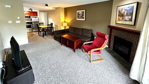 Ein Wohnzimmer mit Sofa, rotem Sessel, Couchtisch, Kamin und einem Essbereich mit Tisch und Stühlen.