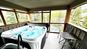 Ein Whirlpool mit Tisch und Stühlen in einem überdachten Außenbereich mit großen Fenstern.