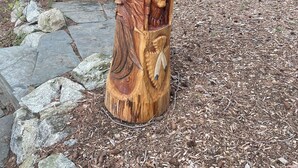 A wooden sculpture of a figure with a conical hat and a carved face, set on a stone base in a wooded area with a wooden structure in the background. - Murphy Bay Lake View Retreat,  Private Deck Oasis, Pet-Friendly (Sandpoint)