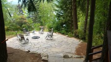 A stone patio with outdoor seating and a fire pit surrounded by trees.