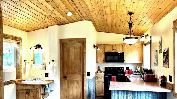 A kitchen with wooden cabinets, a central island with stools, a microwave, and a stove. - Cozy Cabin With Mountain Views (Columbia Falls)