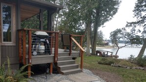 A wooden deck with a stone pathway leading to a house by a lake.