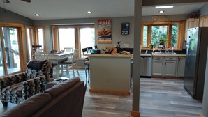 A spacious living area with a large sofa, a dining table, and a kitchen with a refrigerator and wooden cabinets.