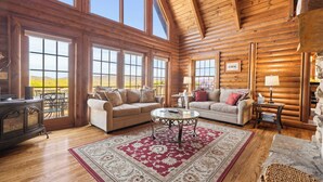 A spacious log cabin with large windows, a cozy living area with a fireplace, and a view of the outdoors. - Stunning Mountain Views on 8 Acres with Hot Tub, sleeps 10 (Saluda)