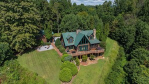 A large log cabin with a green roof, surrounded by dense forest. - Stunning Mountain Views on 8 Acres with Hot Tub, sleeps 10 (Saluda)