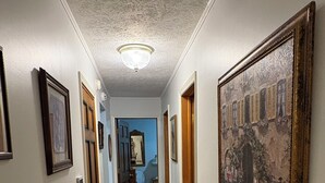 Ein Korridor mit Holzboden, gerahmten Bildern an den Wänden und einem großen Gemälde auf der rechten Seite.