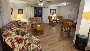 Ein Wohnzimmer mit einer Couch, Sesseln, einem Couchtisch, einem Deckenventilator und einer Soundbox.