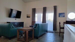 A living room with a sofa, a coffee table, a TV mounted on the wall, and a window with curtains. - Fun by the Sand: Imperial Beach spacious condo steps from the beach!  (Imperial Beach)