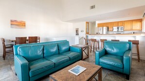 Un salon avec un canapé en cuir turquoise, une table basse en bois et un coin repas comprenant des chaises et une table en bois.