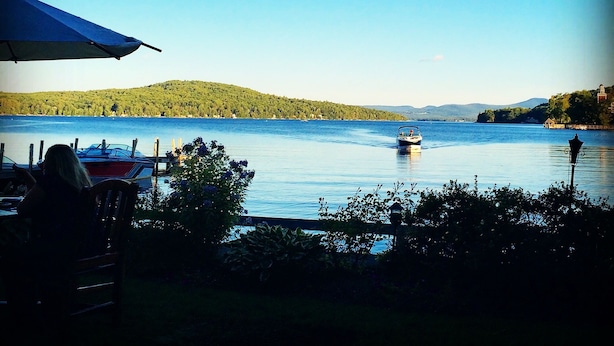 Blick auf ein Seeufer mit einem Boot auf dem Wasser, einem Tisch mit Stühlen und einem Zelt.