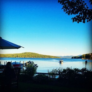 A lakeside view with a boat on the water, a table with chairs, and a tent.