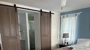 Un dormitori amb un llit, una tauleta de nit, una làmpada i un ventilador de sostre.