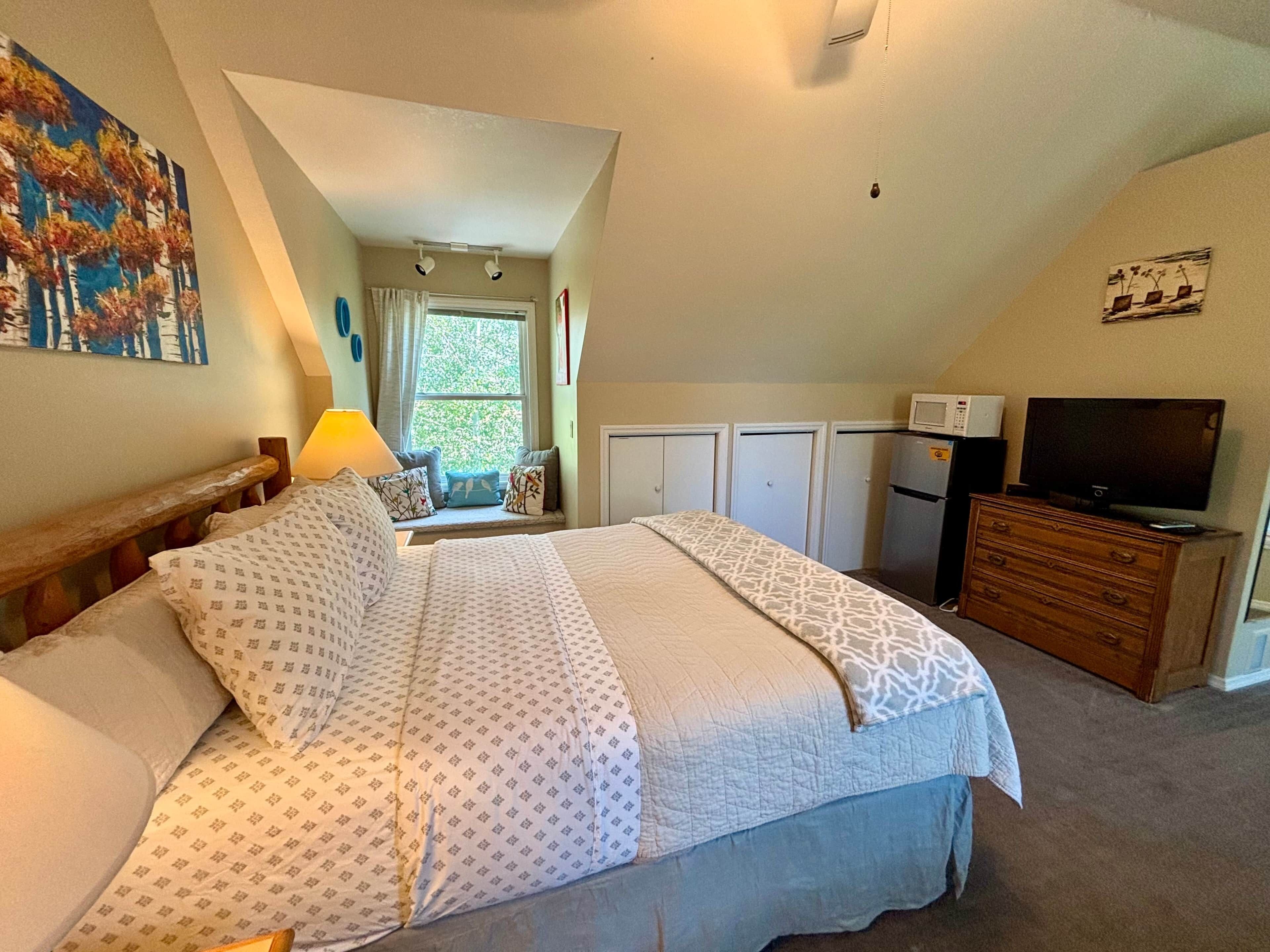 A bedroom with a bed, a dresser, a TV, and a window with curtains.