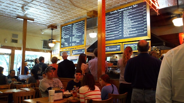 A restaurant interior with wooden tables and chairs, menus on the walls, and people dining. - Well Appointed Home For Your Family's Enjoyment In The Heart of Charlottesville (Charlottesville)