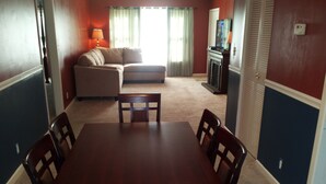 A dining area with a wooden table and chairs, a sofa, and a television in the background. - Well Appointed Home For Your Family's Enjoyment In The Heart of Charlottesville (Charlottesville)