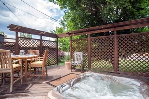 Une terrasse en bois avec un jacuzzi, des chaises et une table.