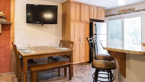 Un espace repas comprenant une table en bois, des chaises et un téléviseur fixé au mur.