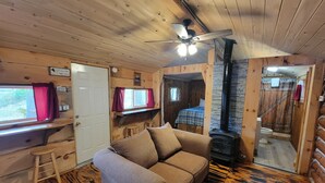 A cozy cabin interior with a wooden floor, a sofa, a desk, a bed, a ceiling fan, and a fireplace.