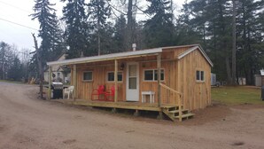 A wooden cabin with a porch, a front door, and a small staircase leading up to the entrance.