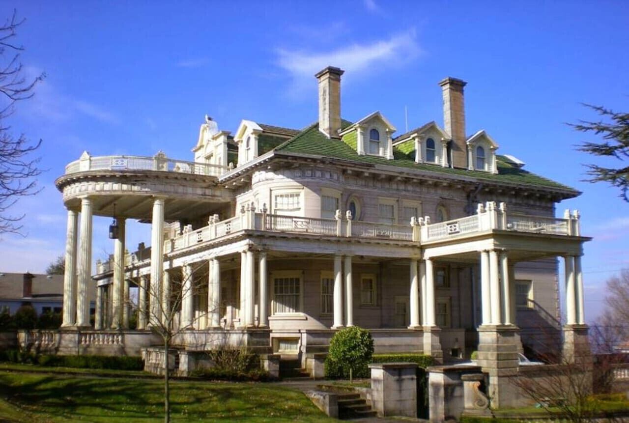 A large, historic building with classical architecture, featuring a central courtyard, multiple wings, and a prominent green roof.