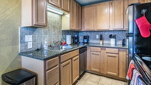 Una cocina con armarios de madera, encimera de granito, lavavajillas de acero inoxidable y refrigerador negro.