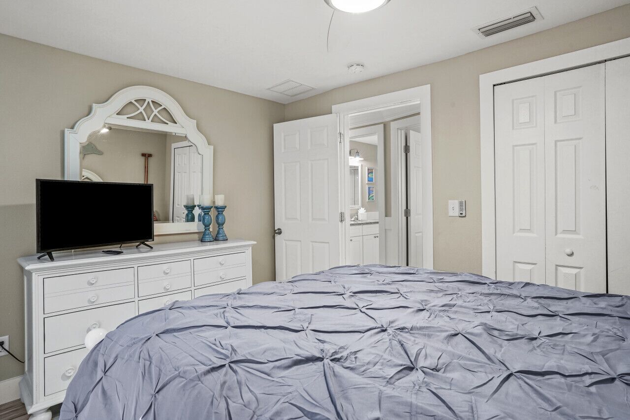 A bedroom with a bed, a dresser, a television, and a mirror.
