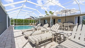 Un espace extérieur abrité comprenant une piscine, des chaises longues et un barbecue.