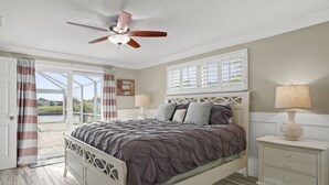Une chambre à coucher comprenant un lit, une table de chevet, un ventilateur de plafond et une fenêtre avec des volets.