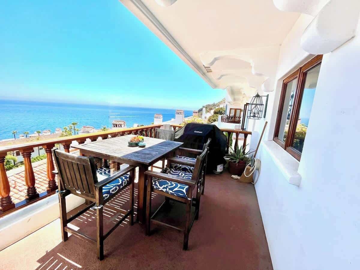 Un balcón con mesa y sillas, una parrilla y vista al océano.