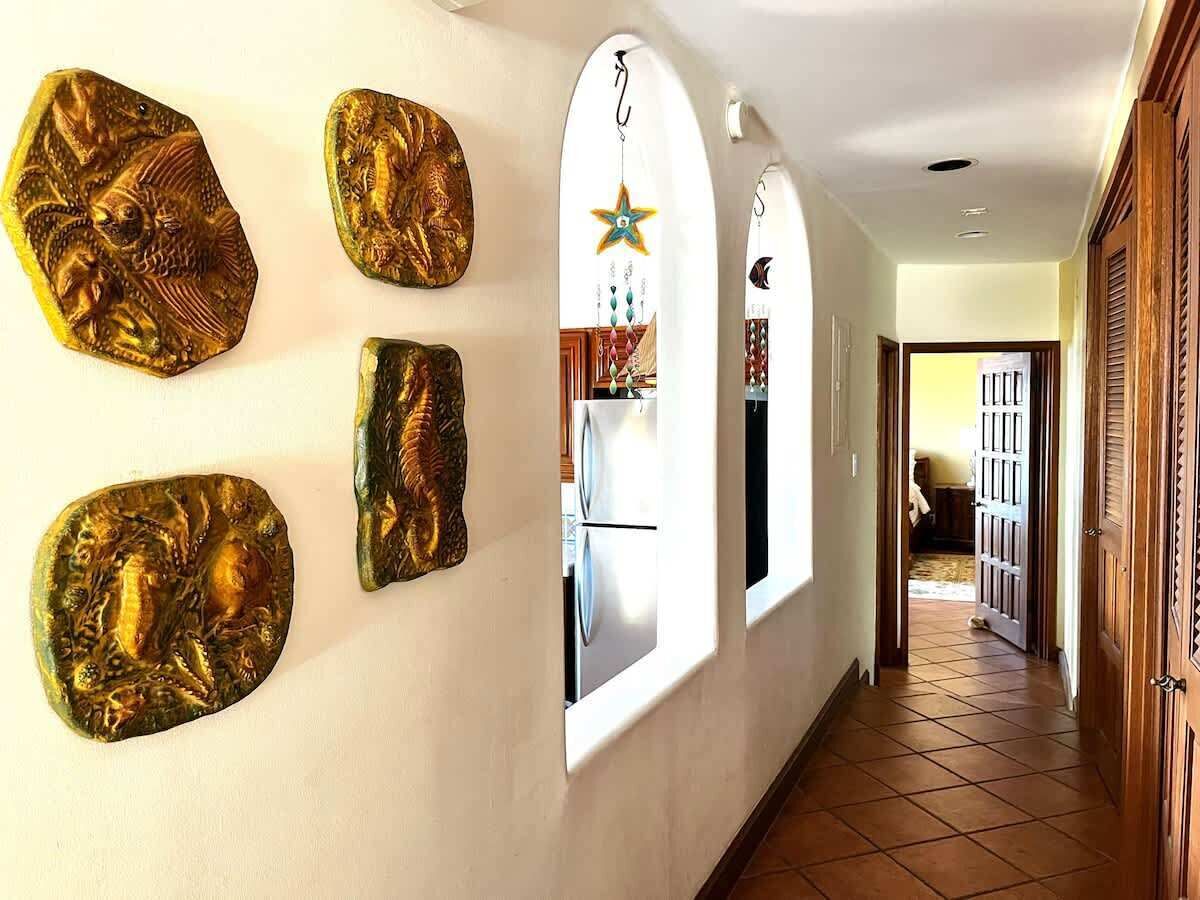 Un couloir agrémenté d’œuvres d’art murales, d’une décoration suspendue en forme d’étoile, et une vue sur une pièce où l’on aperçoit un lit et une fenêtre.