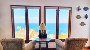 Una stanza con due poltrone a fantasia, un tavolino rotondo con una lampada e ampie finestre vista mare.