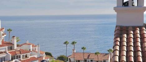 A coastal hotel with multiple balconies, a view of the sea, and palm trees.