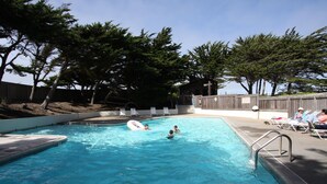 A swimming pool with a wooden deck and lounge chairs, surrounded by trees.