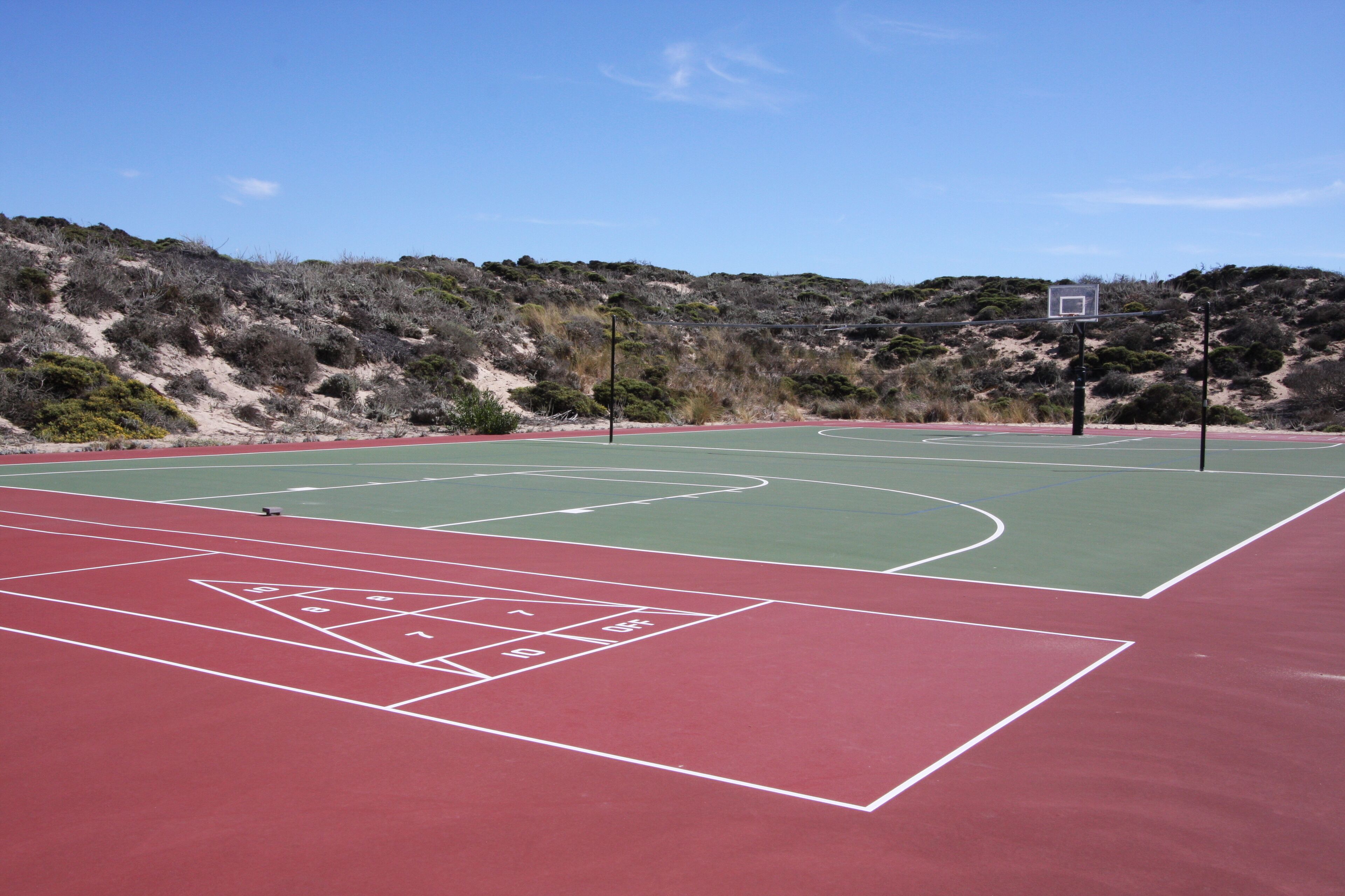Ein Basketballplatz im Freien mit roter und grüner Spielfläche, umgeben von einer hügeligen Landschaft.