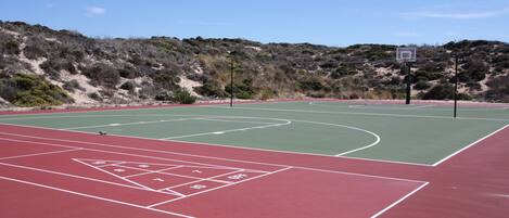 Ein Basketballplatz im Freien mit roter und grüner Spielfläche, umgeben von einer hügeligen Landschaft.