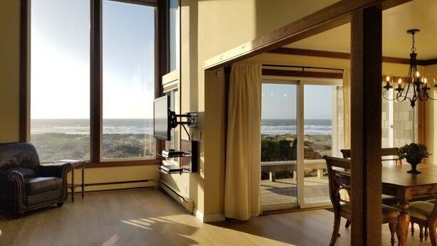A room with a large window overlooking the ocean, a dining area with a chandelier, and a leather armchair.
