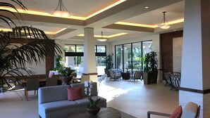Un hall d’entrée spacieux au design moderne, comprenant un canapé, des fauteuils, une table basse et de grandes fenêtres laissant entrer la lumière naturelle.