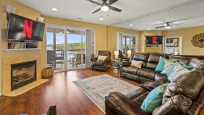 A spacious living room with a fireplace, leather sofas, a large flat-screen TV, and a ceiling fan. - Breathtaking View - Top Floor Lands End Condo, POOL & lazy river! BEST location! (Osage Beach)