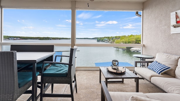 A balcony with a view of a river, wicker furniture, a ceiling fan, and a table with a lantern. - Breathtaking View - Top Floor Lands End Condo, POOL & lazy river! BEST location! (Osage Beach)
